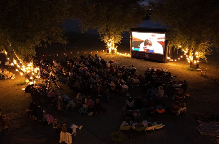 Bezoekers genieten van een openluchtfilm in het Beatrixpark van Almere bij schemering, met het scherm verlicht en Art Playground op de achtergrond.